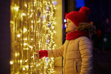 Anaokulu kızı Noel için dekore edilmiş büyük bir mağazanın vitrinine bakıyor. Çocuk Paris, Fransa 'da tatilin tadını çıkarıyor