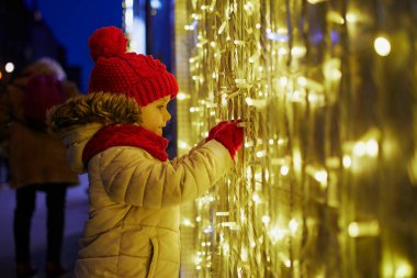 Anaokulu kızı Noel için dekore edilmiş büyük bir mağazanın vitrinine bakıyor. Çocuk Paris, Fransa 'da tatilin tadını çıkarıyor