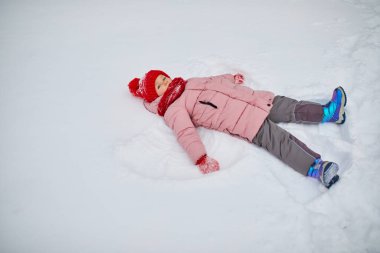 Buz gibi bir kış gününde güzel bir kış parkında kar meleği yapan sevimli anaokulu kızı. Karda oynayan sevimli bir çocuk. Çocuklu aileler için kış etkinlikleri