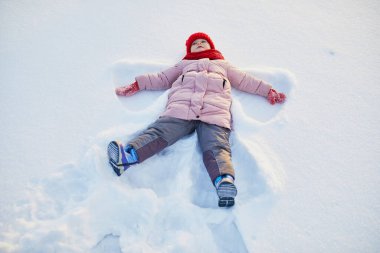 Buz gibi bir kış gününde güzel bir kış parkında kar meleği yapan sevimli anaokulu kızı. Karda oynayan sevimli bir çocuk. Çocuklu aileler için kış etkinlikleri