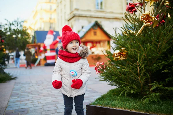 幸せな陽気な就学前の女の子で赤い帽子パリのクリスマスマーケットで楽しんで フランス — ストック写真