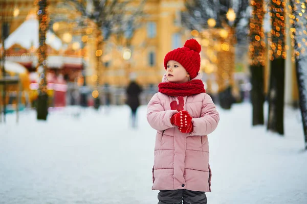 幸せな陽気な就学前の女の子で赤い雪と帽子クリスマスマーケットで楽しみ 鶏形の砂糖ロリポップを食べる — ストック写真