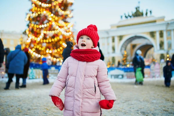 幸せな陽気な就学前の女の子で赤い帽子にクリスマスマーケット — ストック写真