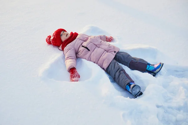 雪の寒い冬の日に美しい冬の公園で雪の天使を作る愛らしい未就学児の女の子 雪の中で遊ぶかわいい子供 子供連れの家族のための冬の活動 — ストック写真