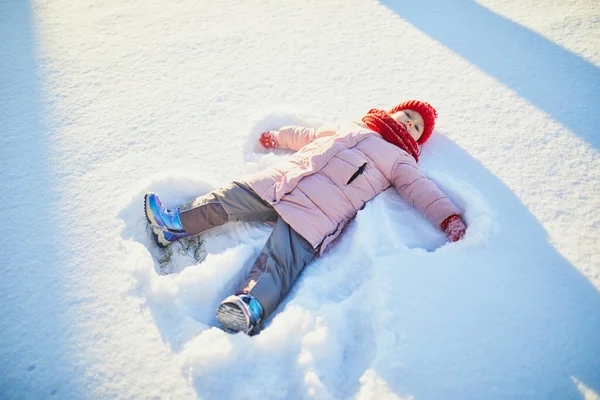 雪の寒い冬の日に美しい冬の公園で雪の天使を作る愛らしい未就学児の女の子 雪の中で遊ぶかわいい子供 子供連れの家族のための冬の活動 — ストック写真