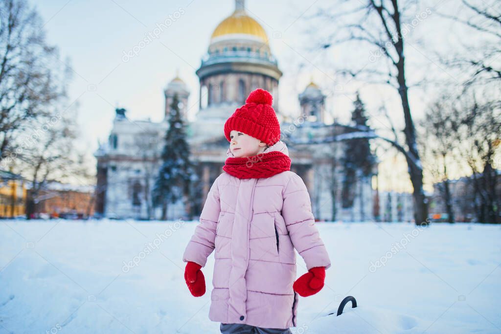 Adorable preschooler girl having fun in beautiful winter park on a snowy cold winter day. Cute child playing in snow. Winter activities for family with kids