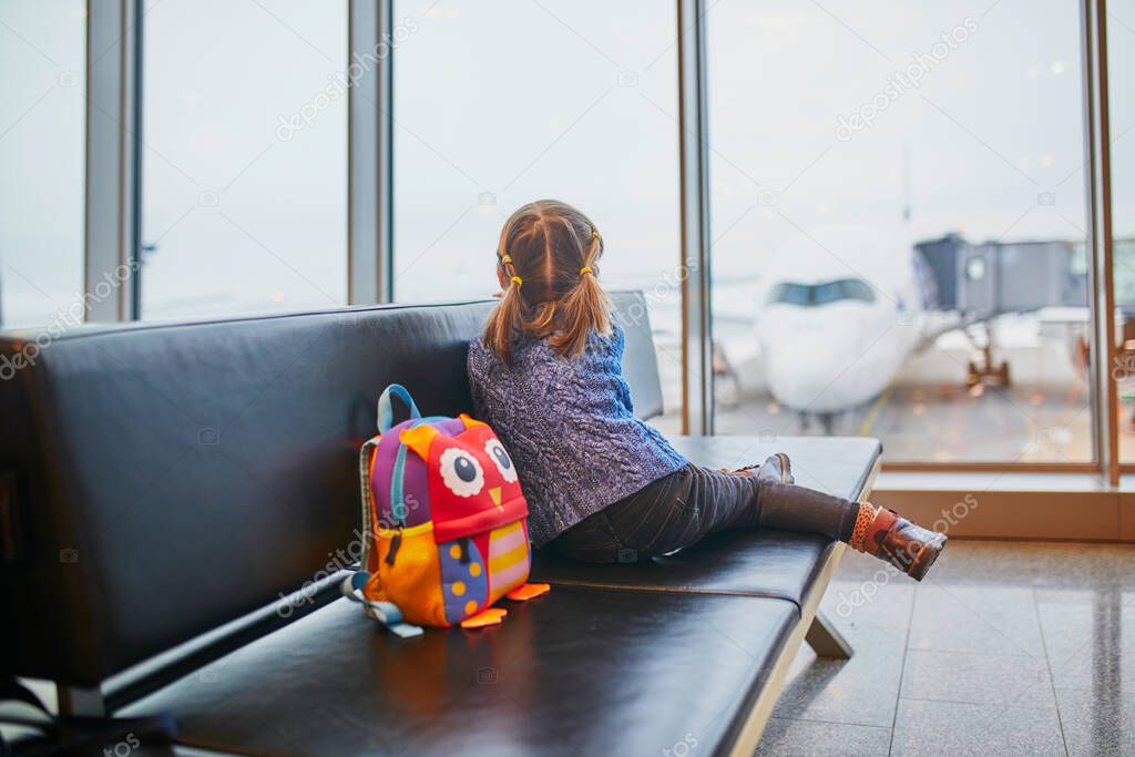 Adorable little preschooler girl traveling by plane. Child sitting in gate and waiting for the flight. Traveling abroad with kids. Unaccompanied minor concept