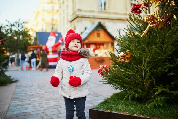 幸せな陽気な就学前の女の子で赤い帽子パリのクリスマスマーケットで楽しんで フランス — ストック写真