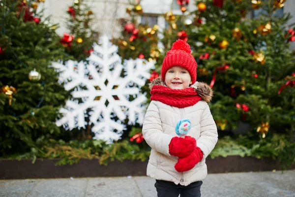 幸せな陽気な就学前の女の子で赤い帽子パリのクリスマスマーケットで楽しんで フランス — ストック写真