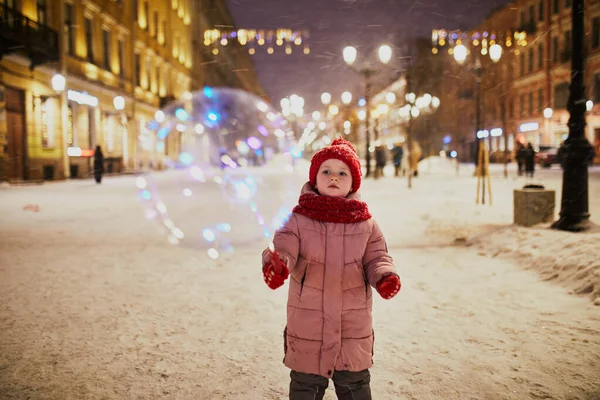 幸せな未就学児の女の子は冬の日に雪と路上で照明された風船で遊んで — ストック写真