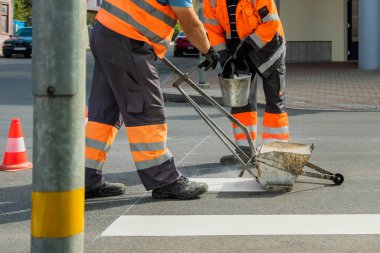 Erkekler yolda çalışıyor, beyaz yaya geçitlerini boyuyorlar..