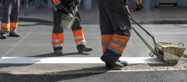 Erkekler yolda çalışıyor, beyaz yaya geçitlerini boyuyorlar..