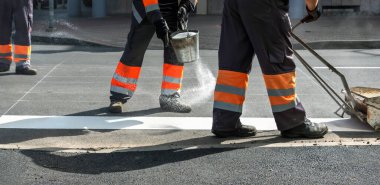 Erkekler yolda çalışıyor, beyaz yaya geçitlerini boyuyorlar..