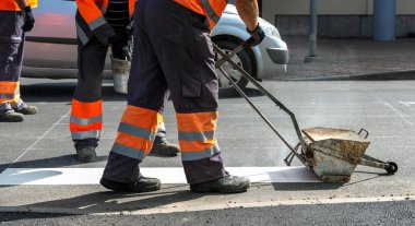 Erkekler yolda çalışıyor, beyaz yaya geçitlerini boyuyorlar..