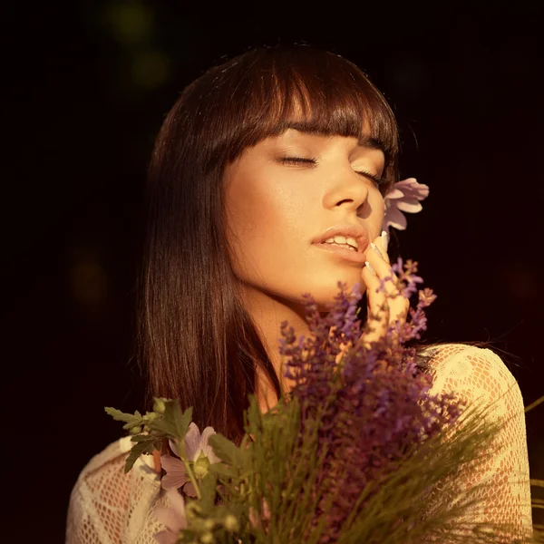 Schöne junge brünette Frau mit Wildblumen in der Hand — Stockfoto