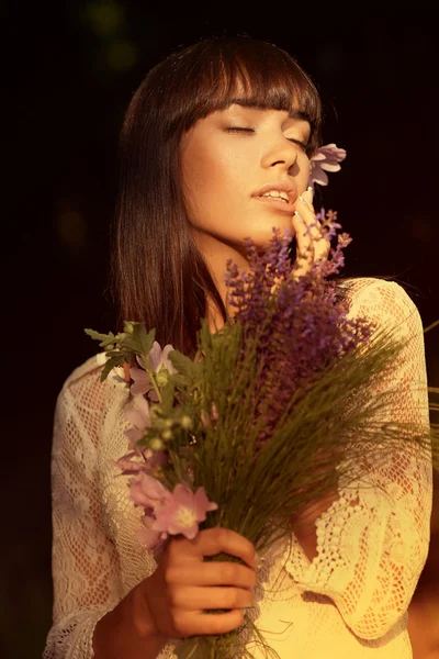 Beautiful young brunette woman with wildflowers in hand — Stock Photo, Image