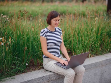 Modern üniversite kampüs parkında dizüstü bilgisayarla çalışan bir kadın..