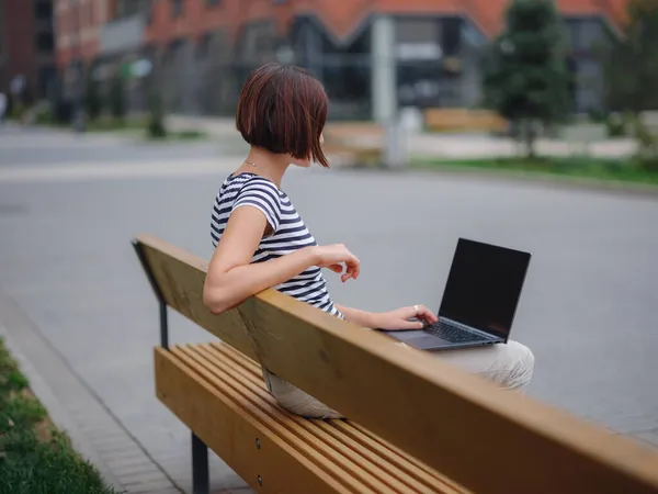 Estudiante trabajando en el ordenador portátil sentarse en el banco en la calle urbana de la ciudad. — Foto de Stock