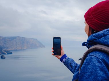 Kadın akıllı telefondan denizin fotoğrafını çekiyor.