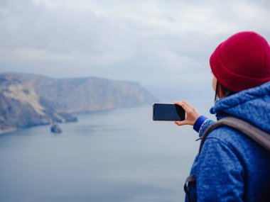 Kadın akıllı telefondan denizin fotoğrafını çekiyor.