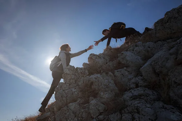 Silhouetten van twee mensen die bergen beklimmen en helpen tegen de blauwe lucht. — Stockfoto