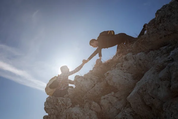 Silhuetas de duas pessoas escalando montanhas e ajudando contra o céu azul. — Fotografia de Stock