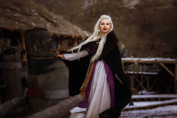 Beautiful blonde Viking dressed in a black cloak against the backdrop of the castle — Stock Photo, Image