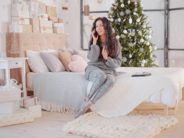 Kadın yatakta oturuyor, cep telefonuyla konuşuyor.