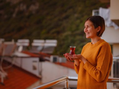 Geleneksel Türk çay fincanından Türk çayı içen kadın, Türkiye 'nin Akdeniz kıyısındaki Kas tatil beldesinin gün batımında manzaranın keyfini çıkarıyor