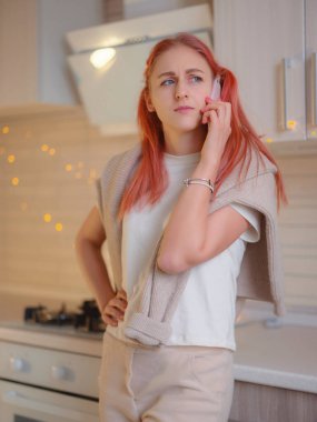 Genç beyaz bir kadın mutfakta cep telefonu kullanıyor. Merkez ofis. Güzel bir bayan internette cep telefonuyla konuşuyor. Üzücü duygular ifade etmek. Sorunlar ve kötü haber kavramı