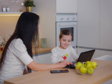Çalışan anne ev ofisinde çalışıyor. Kadın ve çocuk dizüstü bilgisayar kullanıyor. Rahat mutfağındaki Freelancer 'ın işyeri. Kadın işi, nezaket, ilgi. Yaşam biçimi.