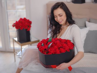 Beyaz elbiseli genç bir kadın yatakta oturuyor. Sabah aşkı yatak odası. Yıldönümü, mutlu yıllar, düğün, aşk günü, kadınlar günü, sevgililer günü ve olumlu duygular.