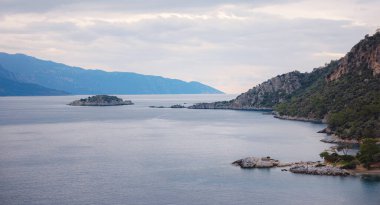 Oludeniz, Fethiye, Türkiye 'deki Lagün' e git. Darbogaz yakınlarında bir plaj. Dağlı kış manzarası, yeşil orman, gök mavisi su, sahil ve bulutlu gökyüzü
