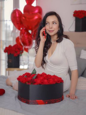 Beyaz elbiseli genç bir kadın yatakta oturuyor. Sabah aşkı yatak odası. Yıldönümü, mutlu yıllar, düğün, aşk günü, kadınlar günü, sevgililer günü ve olumlu duygular.