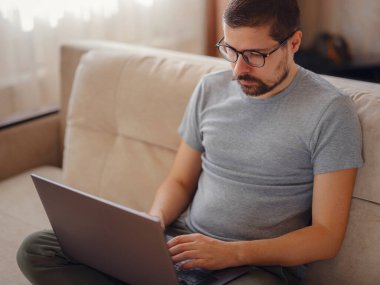 Evde dizüstü bilgisayar kullanan yakışıklı bir genç. Öğrenci erkekler odasında. Çevrimiçi alışveriş, ev işi, serbest çalışma, çevrimiçi öğrenme, öğrenim kavramı. Uzaklık eğitimi