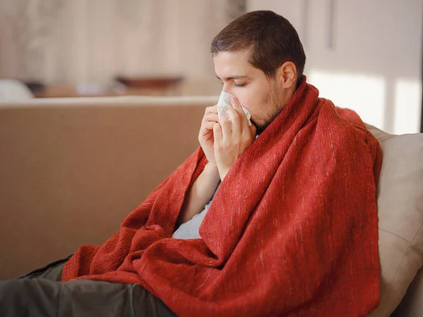 Coronavirus. Corona virüsünün hasta adamı kanepede uzanıyor ve evdeki hastalıktan kurtuluyor. Burnunu siliyor. Yüksek sıcaklık kavramı. Bu kişi çok hasta..