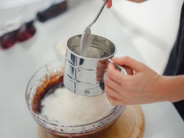 Ev yemeği konsepti. Esmer kadın keki elemek için un eleme, tuzlama hamuru. Genç kadın gülümsüyor, güzel modern mutfakta yemek yapmayı seviyor..