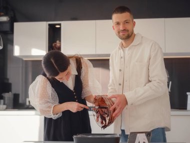 Fırın, yemek ve insan konsepti. Genç çift gülümsüyor. Mutfakta çikolatalı kek pişiriyorlar.