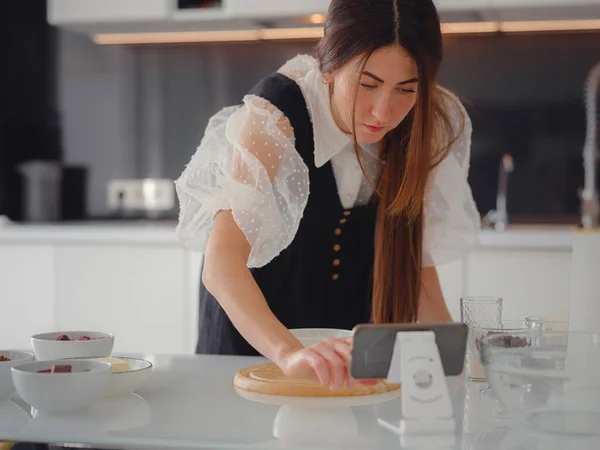 Young woman looks at a recipe for cooking a pie in a smartphone. food tutorial or cooking courses online. Baking dessert concept.