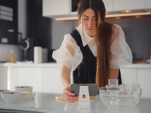 Young woman looks at a recipe for cooking a pie in a smartphone. food tutorial or cooking courses online. Baking dessert concept.
