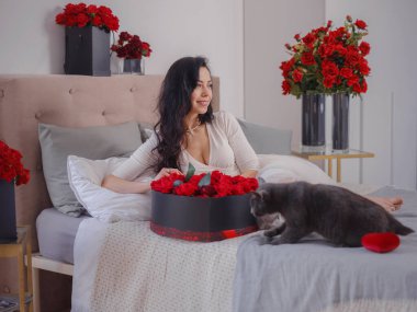 Beyaz elbiseli genç bir kadın yatakta oturuyor..