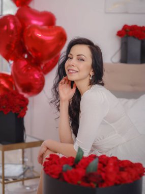 Beyaz elbiseli genç bir kadın yatakta oturuyor. Sabah aşkı yatak odası. Yıldönümü, mutlu yıllar, düğün, aşk günü, kadınlar günü, sevgililer günü ve olumlu duygular.