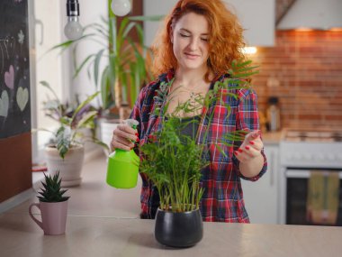 Ekose gömlekli gülümseyen kadın bahçıvan bitkilerle ilgileniyor. Evde bahçıvanlık, ev bitkisi sevgisi, serbest çalışma. Evde bahçıvanlık ve yavaş yaşam ritüelleri. Kapalı alanda bahçe işleri..