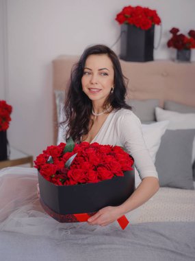 Beyaz elbiseli genç bir kadın yatakta oturuyor. Sabah aşkı yatak odası. Yıldönümü, mutlu yıllar, düğün, aşk günü, kadınlar günü, sevgililer günü ve olumlu duygular.