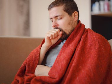 Coronavirus. Corona virüsünün hasta adamı kanepede uzanıyor ve evdeki hastalıktan kurtuluyor. Burnunu siliyor. Yüksek sıcaklık kavramı. Bu kişi çok hasta..