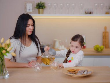 Evde mutfakta kurabiyelerle çay içen bir aile. Anne ve kızı evde birlikte mutlu bir an geçiriyorlar..