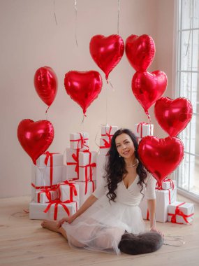 Beyaz elbiseli ve gri kedili güzel, mutlu genç bir kadın. Tatil partisi. Kırmızı kalp şeklinde balonlarla poz veren neşeli manken, eğlenen, Sevgililer Günü 'nü kutlayan. Aşkın sembolü