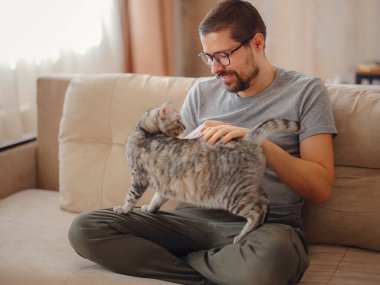 Sahibi oturma odasında kanepede dinlenirken kediyle oynuyor. Genç bir adam evde evcil hayvanla dinleniyor. Evcil hayvan konsepti