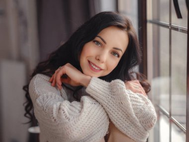 Beautiful young woman near window at home. Free Time To Relax. Happy lady taking break near window