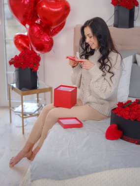 Gülümseyen mutlu kadın, hediye kutusuyla telefonda sevdikleriyle konuşuyor, yatakta oturup kameraya bakıyor. Sevgililer Günü 'nün kutlaması, düğün ve aşk günü, kadınlar günü. Sabah aşk yatak odası.